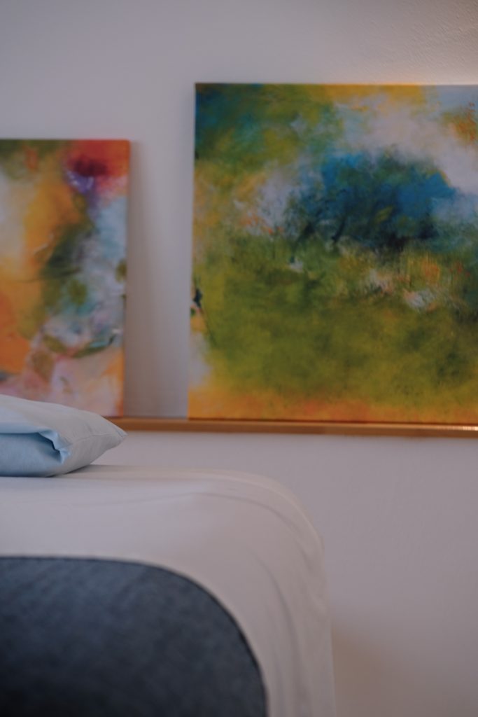 Massageliege mit blauer Decke und Kissen vor farbenfrohen Praxisbildern – harmonisches Ambiente für die Ganzheitlich Energetische Massage